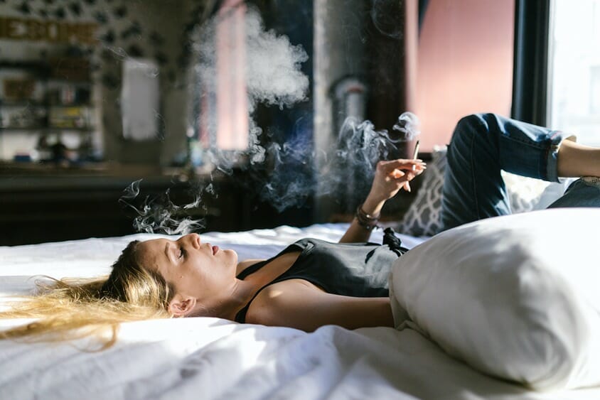 Woman lying on a bed smoking a CBD joint