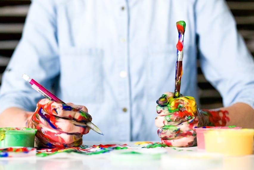 A man holding paintbrushes filled with paint of all colors showing his creative side